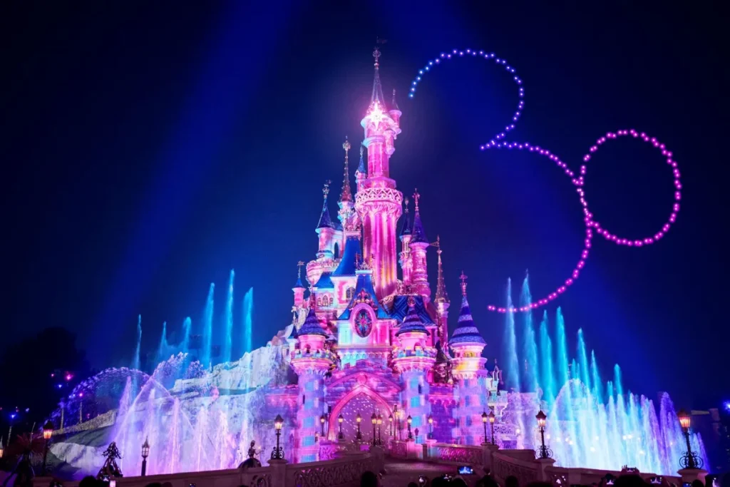 Le château de Disneyland Paris illuminé la nuit, avec feux d’artifice.